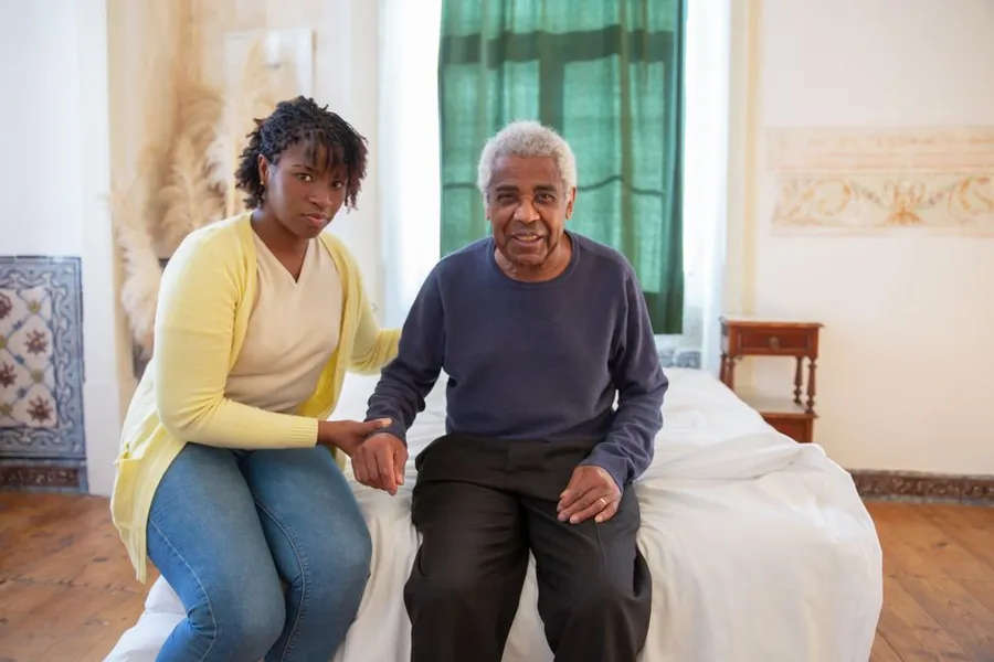 An adult daughter sitting with her elderly father in a bright room