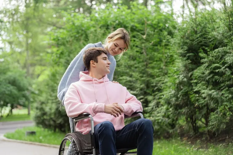 A woman leaning down to talk with a man using a wheelchair in a park